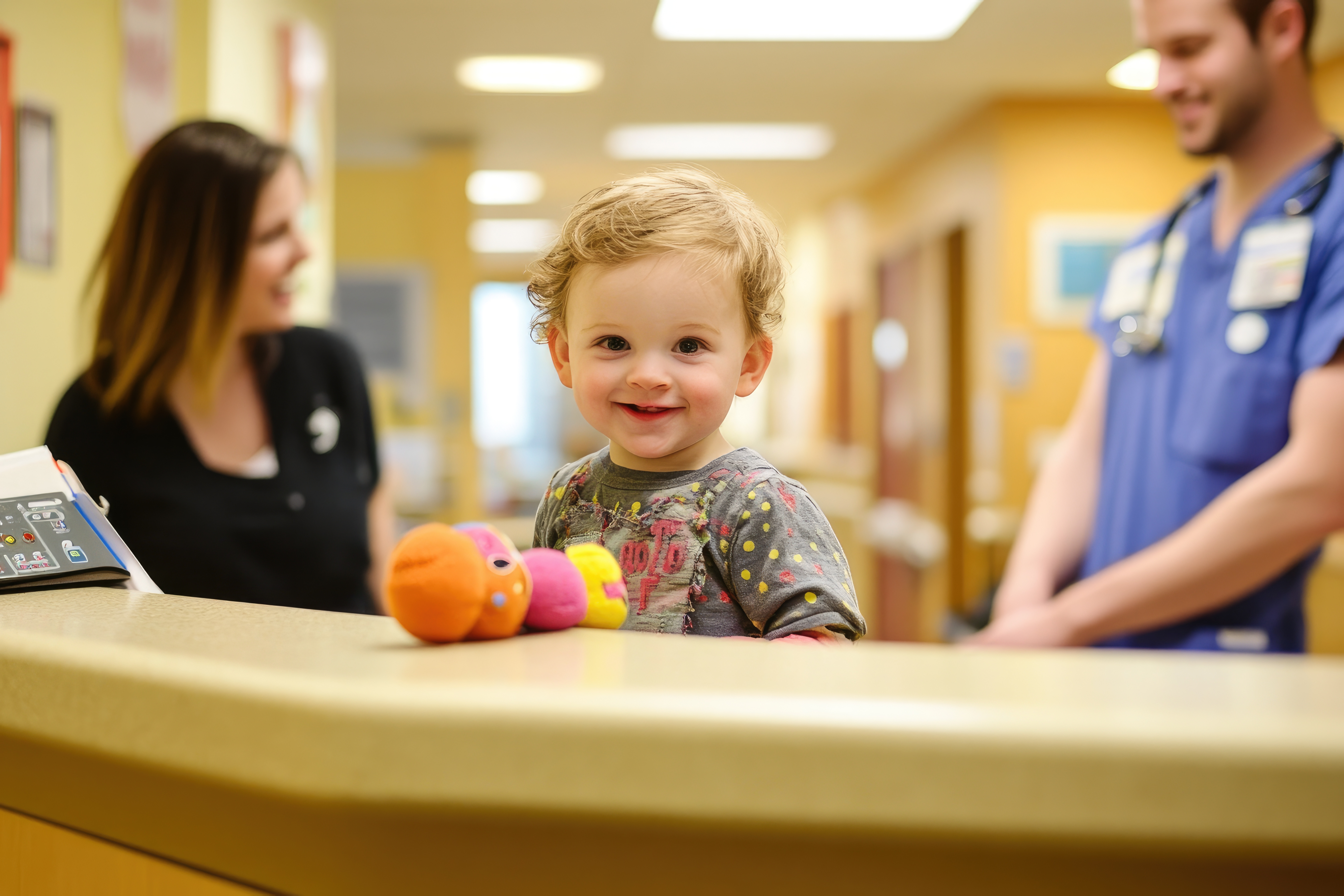 Smiling baby with stuffed animal and smiling nurses in background at clinic