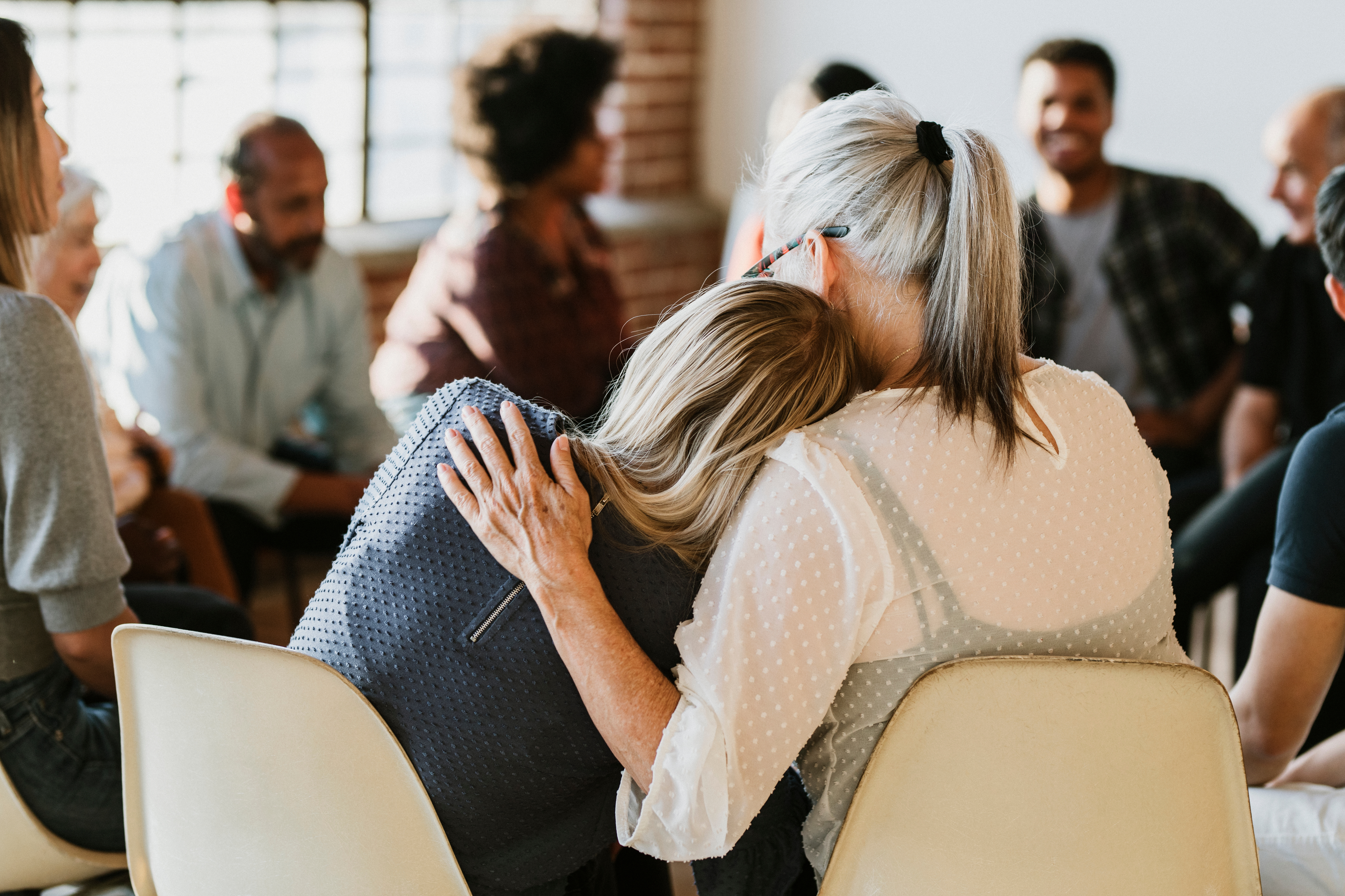 Two women comfort each other in a group therapy session