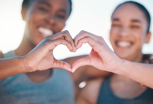 Two smiling women form a heart shape with their hands