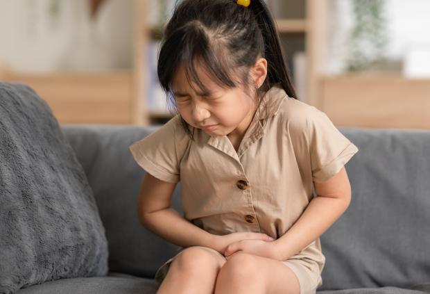 A young girl on a couch appears to have stomach/abdominal pain