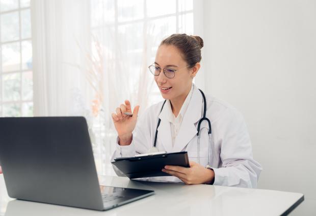 Smiling doctor greets patient on a virtual visit with her laptop