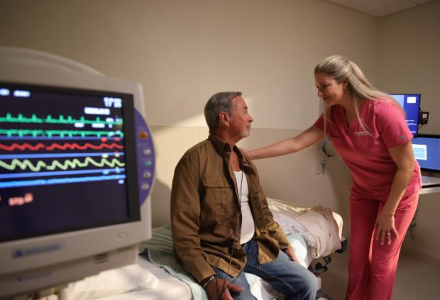 A nurse reassures a patient with heart monitor in foreground.