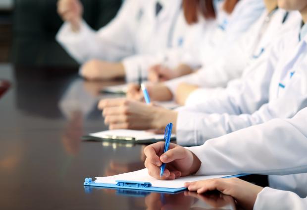 Stock image of white-coated doctors taking notes on clipboards at a table
