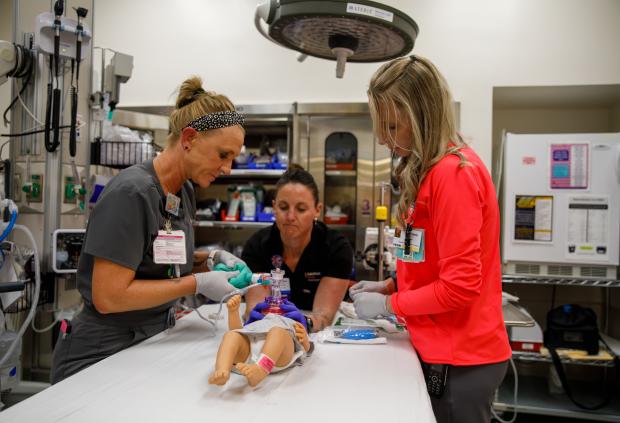 Three healthcare workers in a Saint Francis Hospital ER bay practice with a dummy