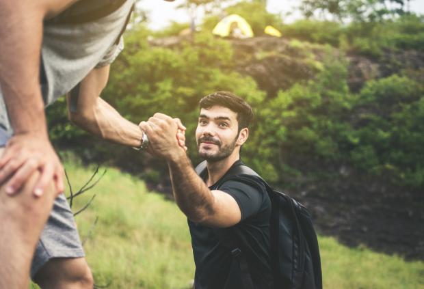 Young man backpacking gets helping hand climbing; overcoming obstacle
