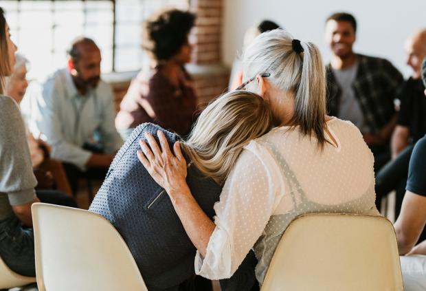Two women comfort each other in a group therapy session