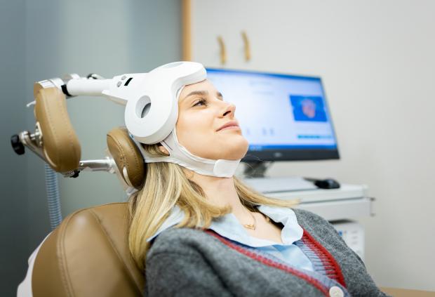 a young woman wearing TMS headgear smiles in a clinical setting