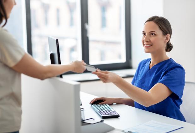 A patient hands a receptionist their insurance card in a doctor's office