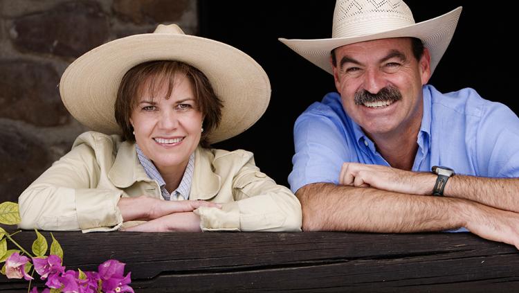 Couple in Cowboy hats looking happy over a fence.