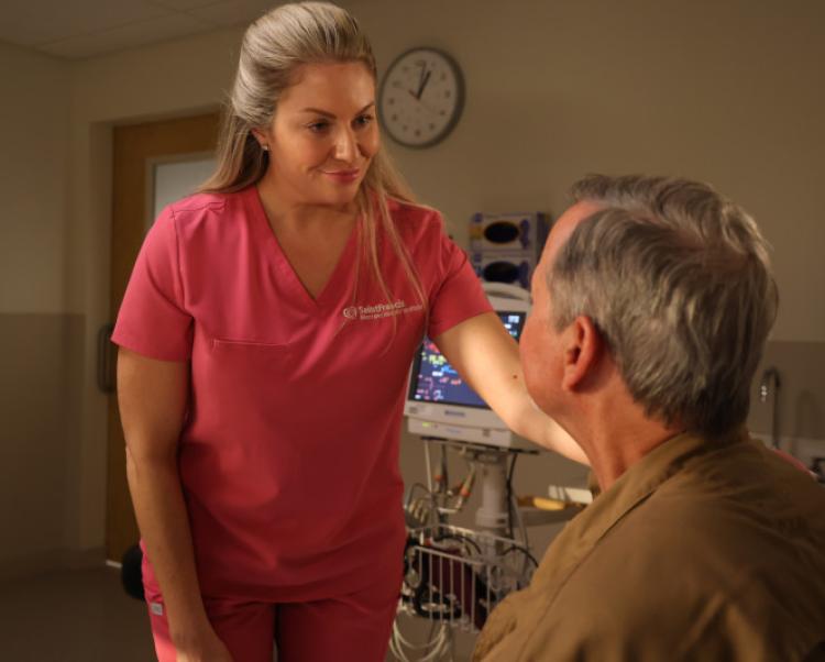 Female nurse in pink scrubs reassures seated patient in clinic