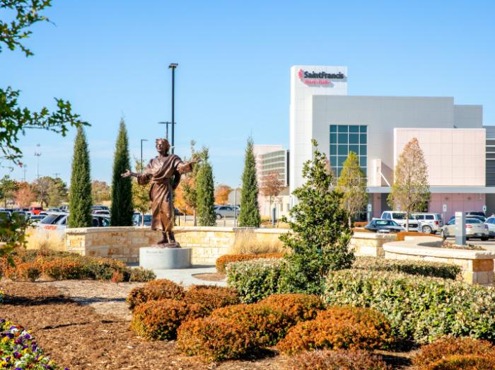 Exterior view of Saint Francis Cancer Center with garden and dancing Jesus statue in foreground.