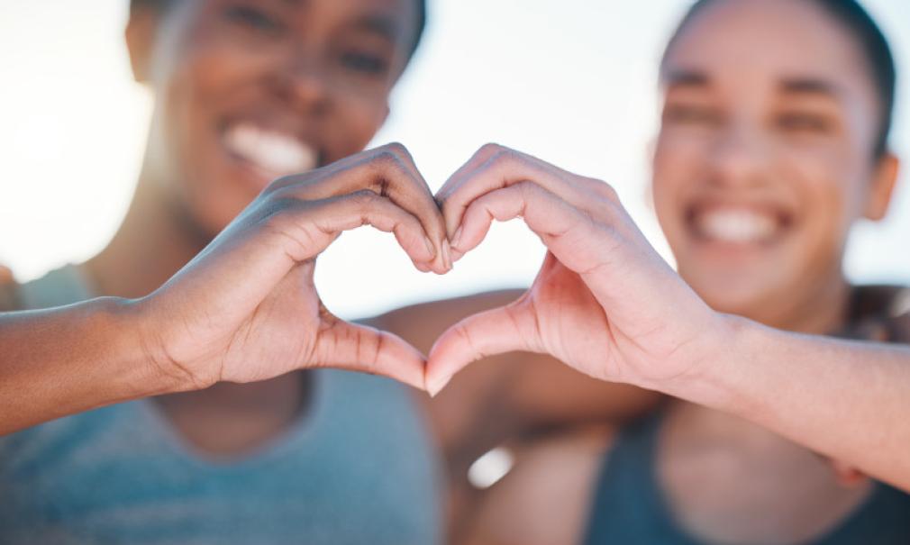 Two smiling women form a heart shape with their hands