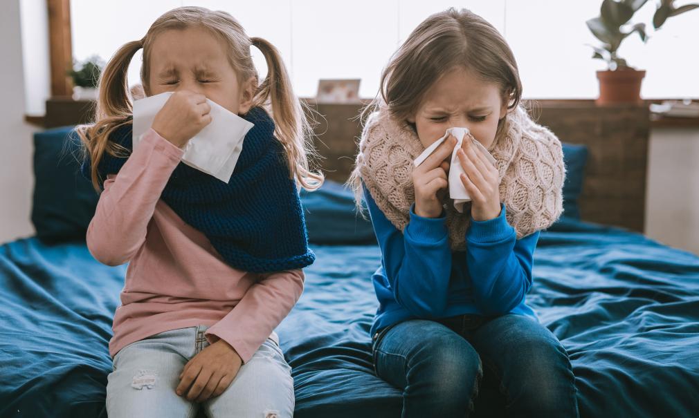 Two young girls use tissues to blow their noses