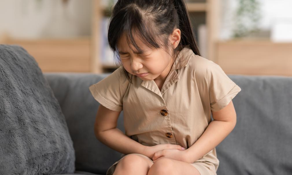 A young girl on a couch appears to have stomach/abdominal pain