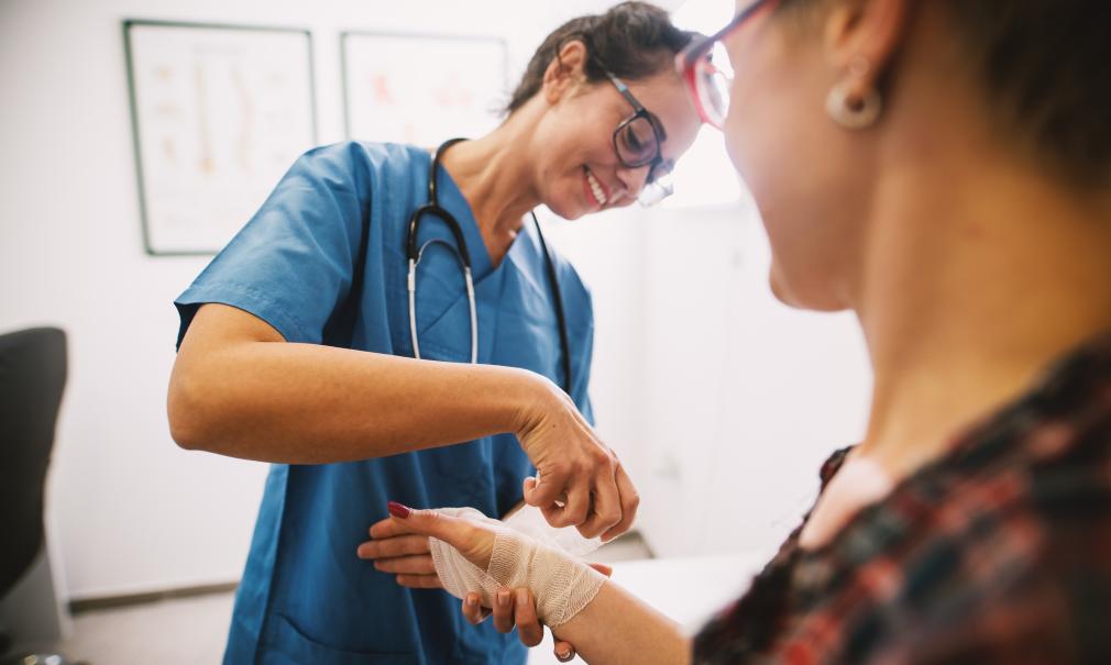 Smiling nurse applies bandage to patient's hand