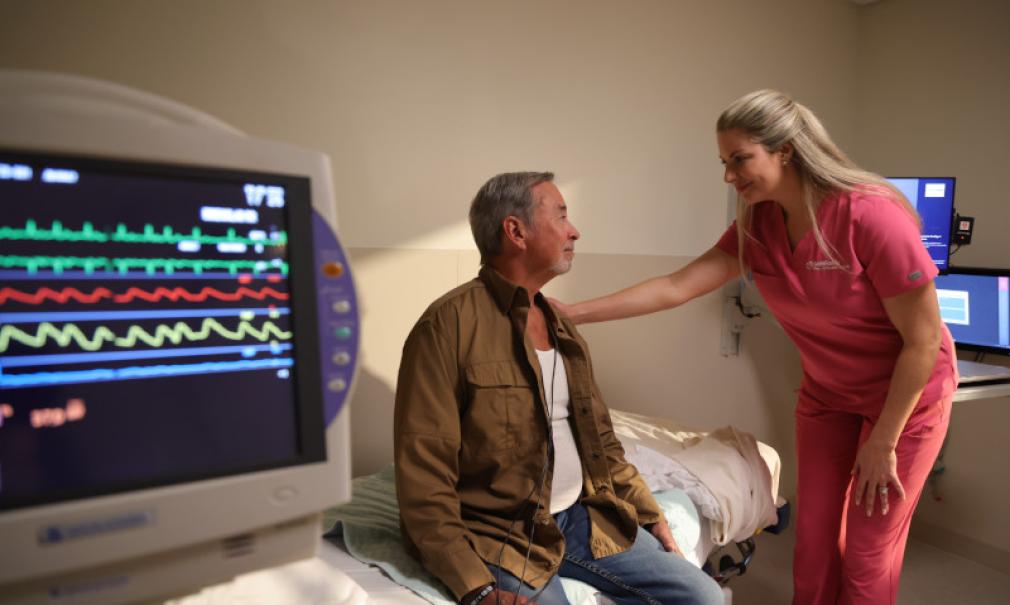 A nurse reassures a patient with heart monitor in foreground.