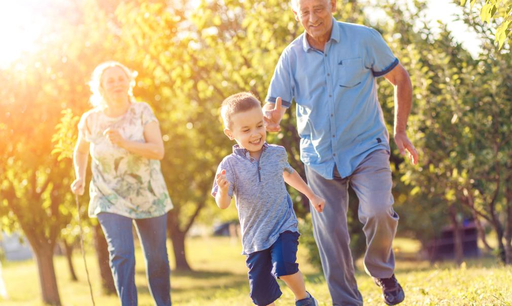 mature couple in sunny meadow chases laughing grandson