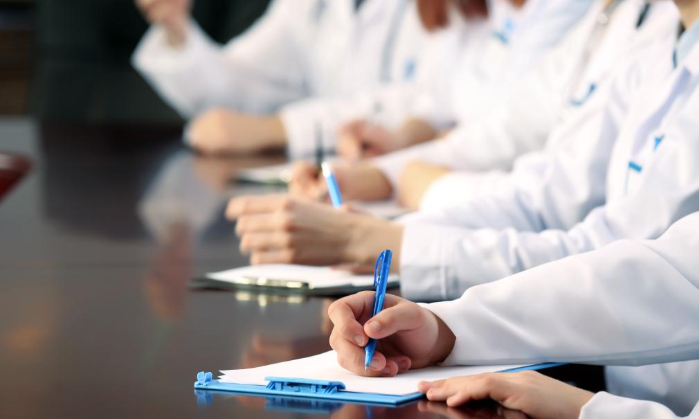 Stock image of white-coated doctors taking notes on clipboards at a table