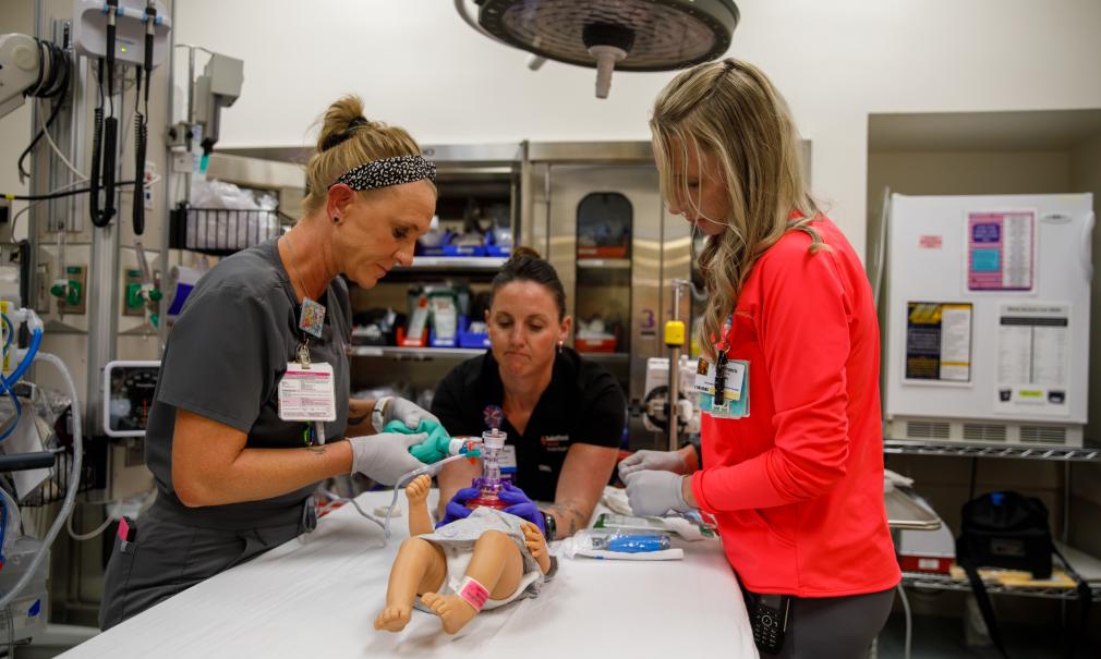 Three healthcare workers in a Saint Francis Hospital ER bay practice with a dummy