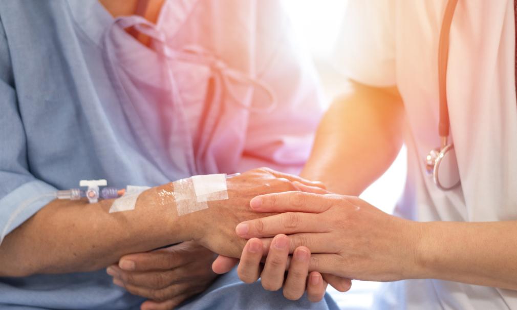 Closeup image of a doctor's hand holding patient's hand in comforting way