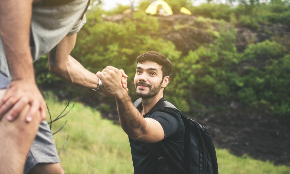 Young man backpacking gets helping hand climbing; overcoming obstacle