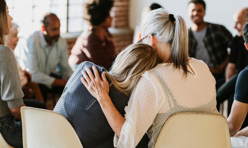 Two women comfort each other in a group therapy session