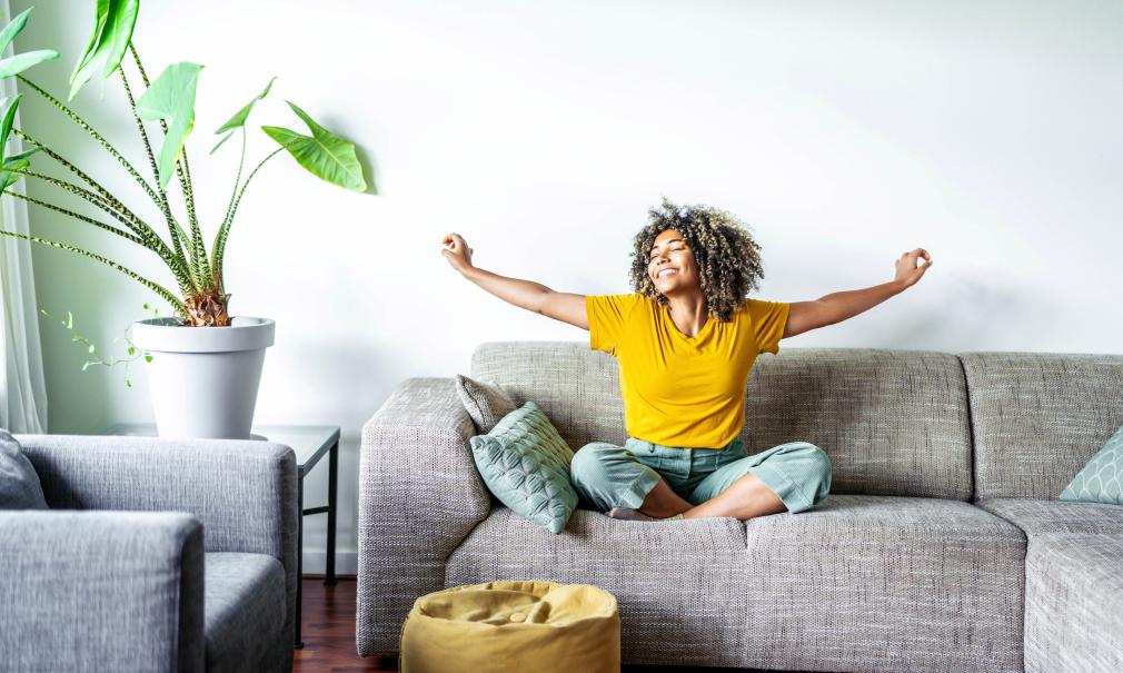 Woman smiles and stretches her arms in a cozy sunlit living room