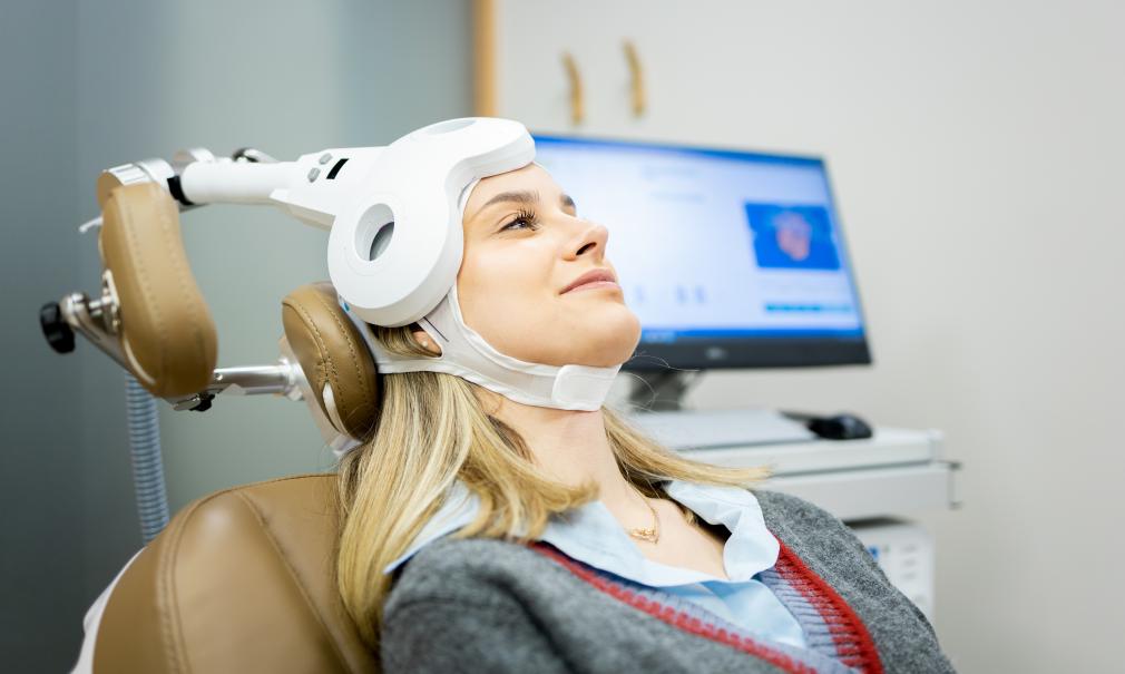 a young woman wearing TMS headgear smiles in a clinical setting