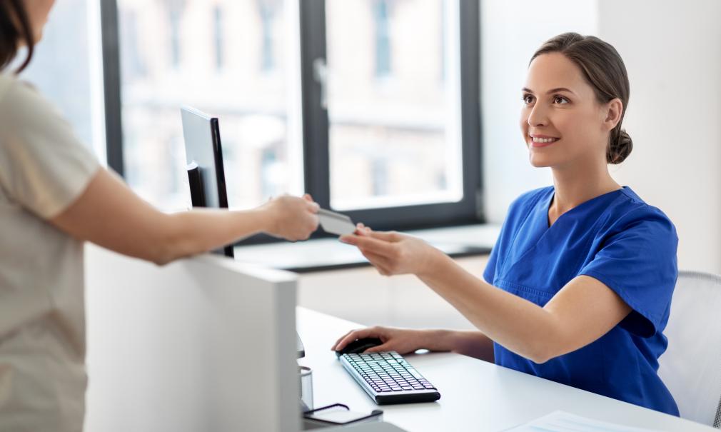 A patient hands a receptionist their insurance card in a doctor's office