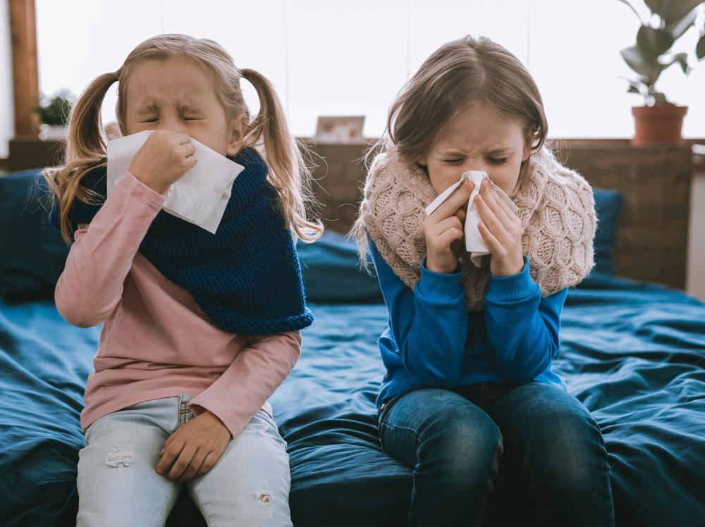 Two young girls use tissues to blow their noses