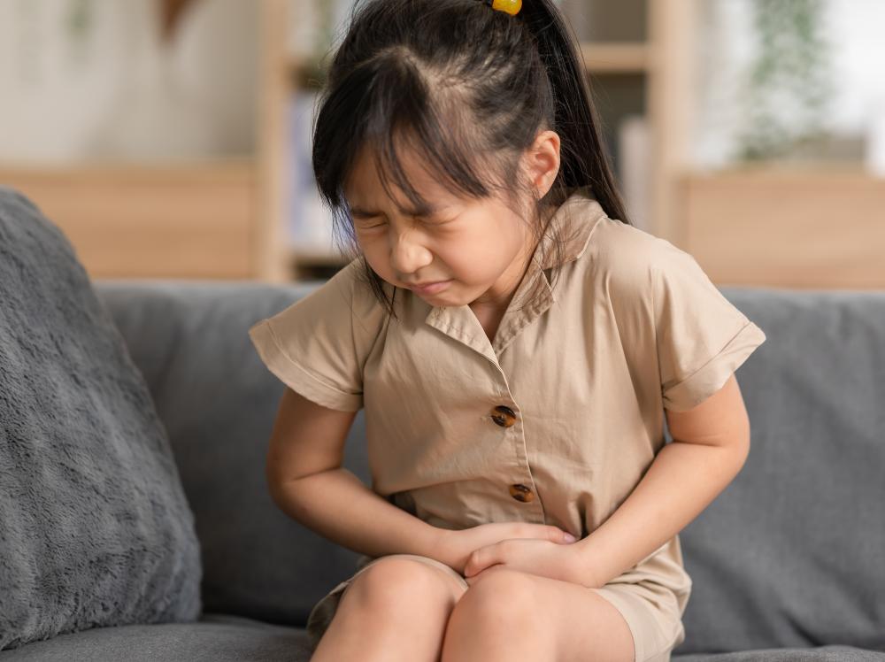 A young girl on a couch appears to have stomach/abdominal pain