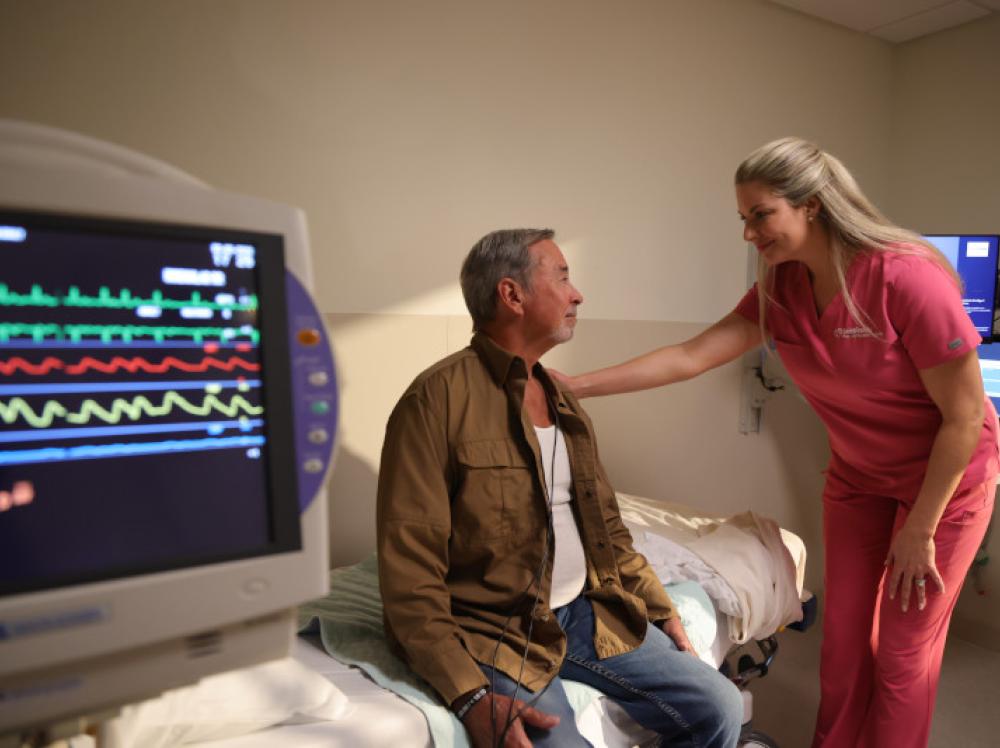 A nurse reassures a patient with heart monitor in foreground.