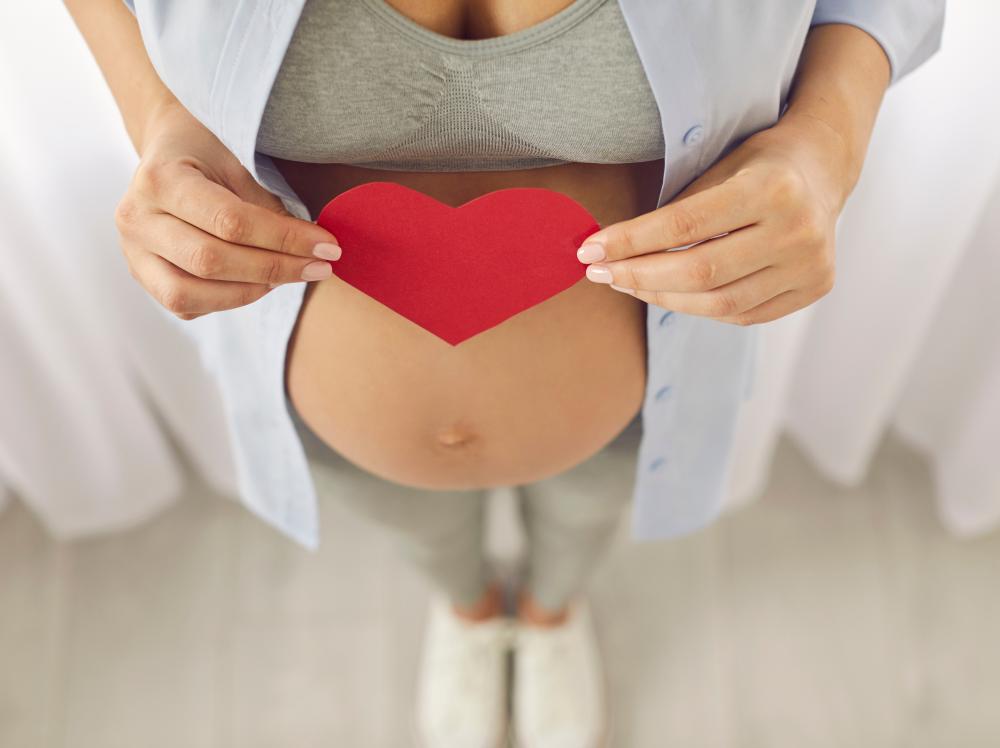 Closeup of a pregnant mother holding a red heart-shaped card over her baby bump