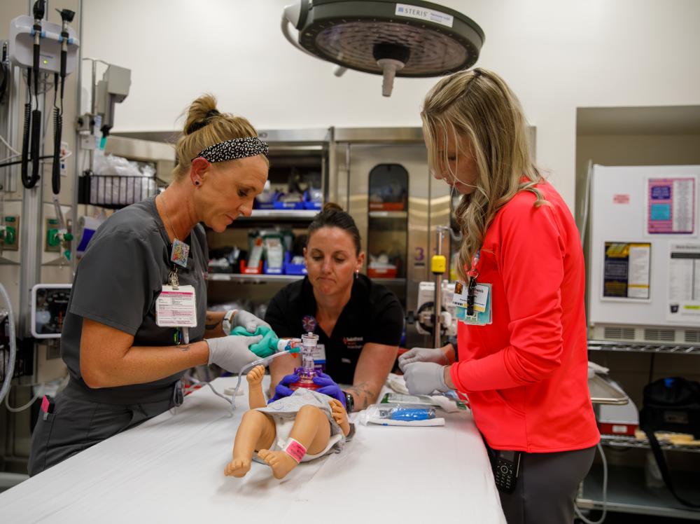 Three healthcare workers in a Saint Francis Hospital ER bay practice with a dummy