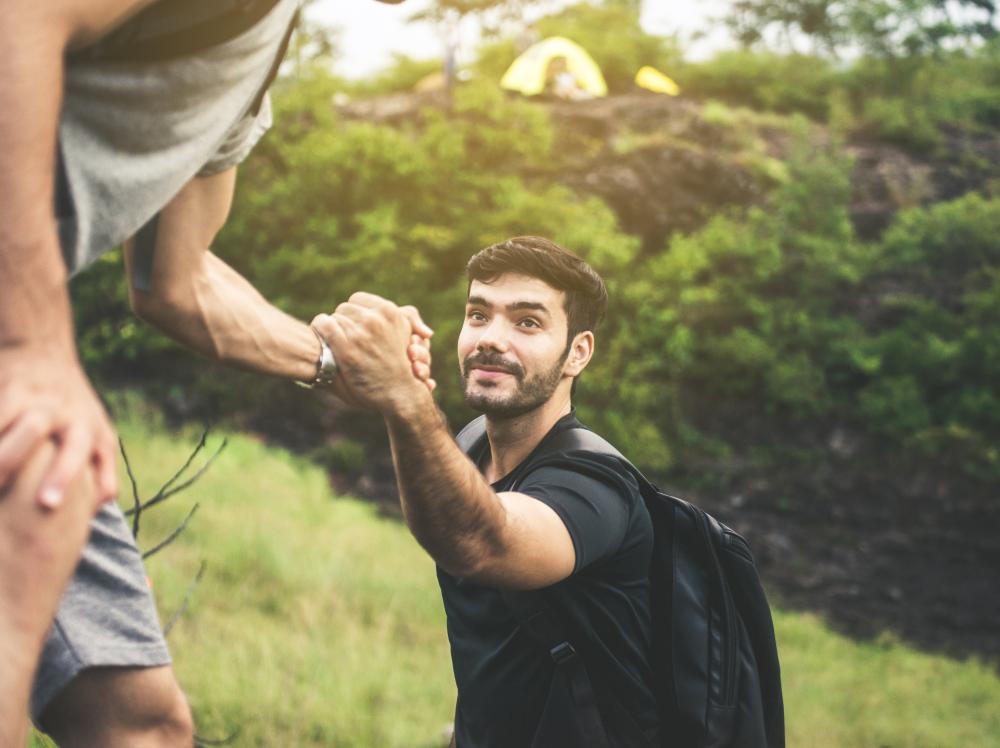 Young man backpacking gets helping hand climbing; overcoming obstacle