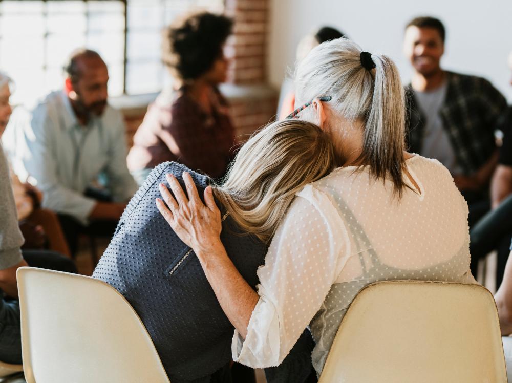 Two women comfort each other in a group therapy session