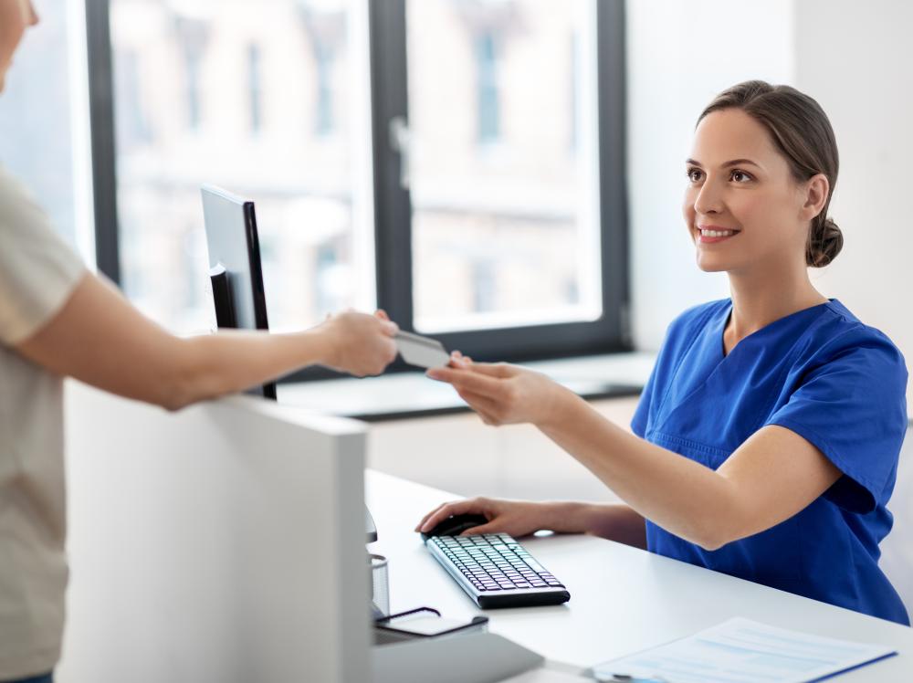 A patient hands a receptionist their insurance card in a doctor's office
